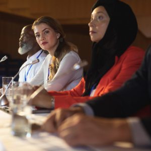 Side view of blonde Caucasian businesswoman looking at camera while business colleague sitting together in the auditorium